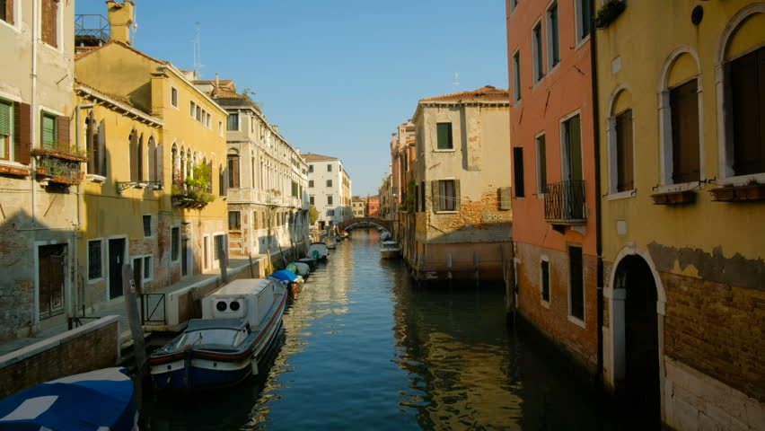 A scenic view of a beautiful Venetian canal on a sunny day with colourful reflections of houses and boats running along the water in the town of Venice, Italy. Still shot in 4k.