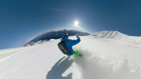 FOLLOW: Extreme freeride snowboarder shredding pristine snow in remote mountain terrain. Snowboarder heliskiing fresh powder snow high in the sunny mountains. Pro rider heliboarding off piste slopes