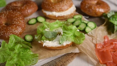 Female hands make a sandwich with a fresh homemade bagel and smoked salmon and low fat cream cheese and cucumber. Healthy breakfast food on rustic wooden background