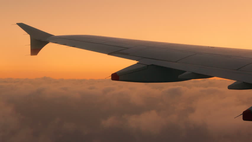 Passengers view of an airplane wing as the plane soars in high altitude during sunset under a blanket of volumetric gray clouds Royalty-Free Stock Footage #1020490315