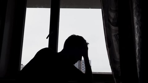Silhouette of desperate sad man in the dark in front of a window