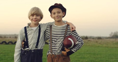 Portrait shot of the two Caucasian teen boys friends players of american football standing with a ball and embracing each other on the field of the countryside, looking at each other with smiles and Vídeo Stock