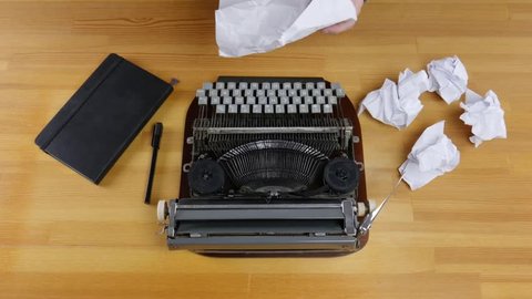 Typewriter, notebook and crumpled sheets of paper on a wooden table. Male hands hold a piece of paper and then throw it away.