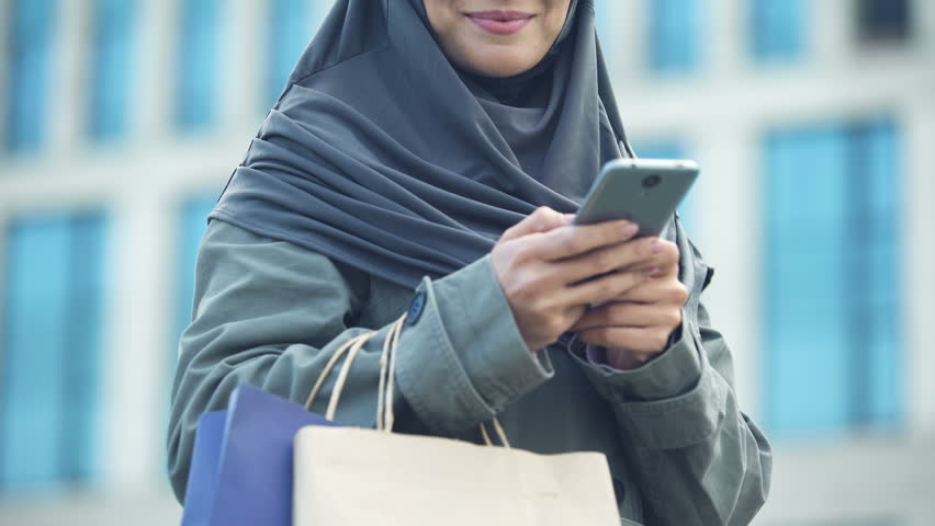 Smiling Arabic lady outdoors chatting on phone after successful shopping fashion