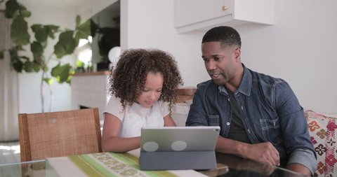 African American father helping daughter with homework using digital tablet