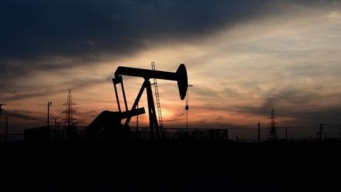 Silhouette of crude oil pump in the oilfield at cloudy sunset