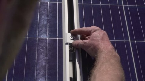 Installing Solar Panels Renewable Energy on a summer day. Hand holding a screw ready for screwing into fabricated metal. 