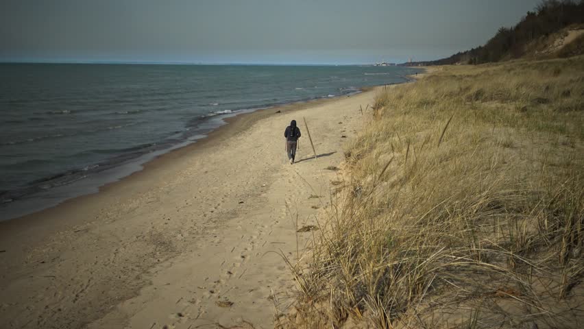 A pedestrian walks along the shore of the lake along the sand dunes