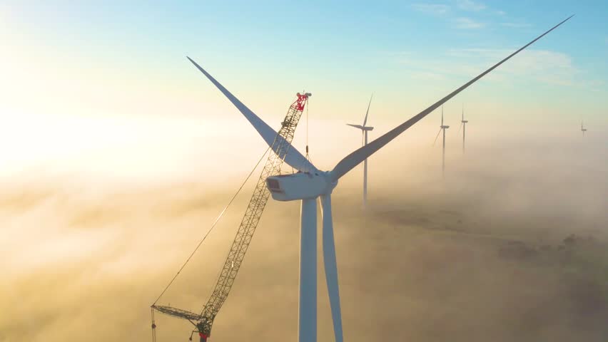 AERIAL: Crane maintaining wind turbine in early morning light Royalty-Free Stock Footage #1020523378