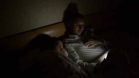 Young couple with smartphone and tablet lying on bed late at night at home