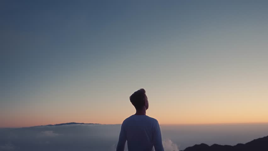 Conceptual video of the winner . A man raises his hands up, standing on a mountain top, above the clouds and blowing strong wind Royalty-Free Stock Footage #1020525874