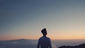 Conceptual video of the winner . A man raises his hands up, standing on a mountain top, above the clouds and blowing strong wind