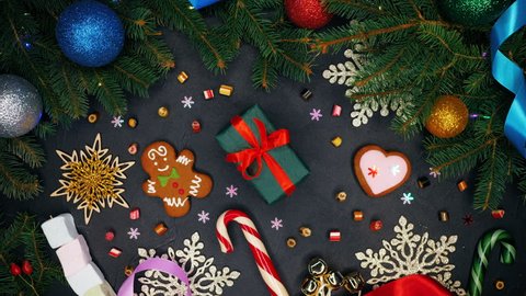 Female hands puts gift wrapped in emerald paper with red ribbon on monochrome surface and then takes it. Black table with Christmas decorations - gingerbread, snowflakes, lollipops.Top plan view