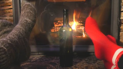A man and a woman drink alcohol at the fireplace from the glasses. The couple celebrate Christmas and New Year. Romantic place for lovers. 
Boyfriend and girlfriend celebrate the anniversary