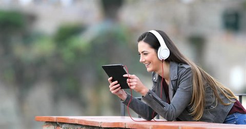 Happy woman watching and listening media in a tablet in a rural apartment terrace