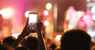 Silhouette of young man holding smartphone in hands, making video of concert. Favorite rock band. Video shooting. Outdoors. Crowd, light effect.