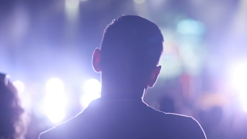 Close-up portrait of guy at music festival. Back shot of young Caucasian man. Silhouettes of crowd of fans in forefront. Sound, music, night. Royalty-Free Stock Footage #1020531268