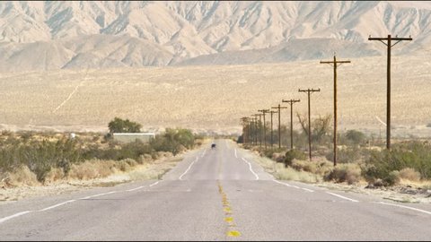 Long shot of a far away minivan driving down a hot desert road with mountains in the background.