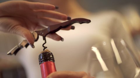 Girl pulls the cork from a wine bottle with a corkscrew close-up. A girl with a beautiful manicure uncorking bottle of wine.