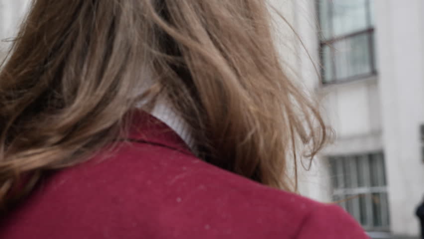 Portrait of attractive bearded hipster man in red fashion coat. Thoughtful and resolute look in big town. Modern businessman model with long hair. Slow motion.Walking away from camera and turn around