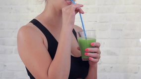Happy woman after fitness is holding green smoothie and drinking it, slow motion video