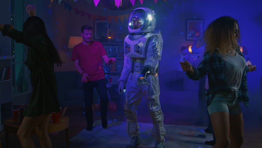 At the College House Costume Party: Fun Guy Wearing Space Suit Dances Off, Doing Groovy Funky Robot Dance Modern Moves. With Him Beautiful Girls and Boys Dancing in Neon Lights. In Slow Motion.