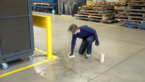 A worker cleans up a puddle of water on a factory floor that is a safety hazard.  An industrial safety topic.