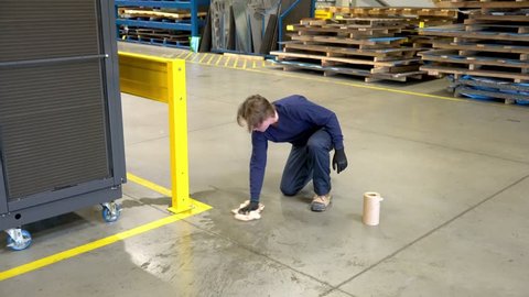 A worker cleans up a puddle of water on a factory floor that is a safety hazard.  An industrial safety topic.