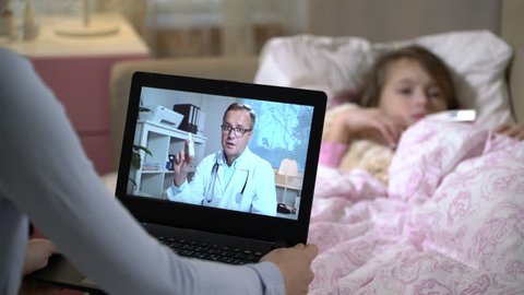 Medicine online. Home quarantine coronavirus. Mom with a little sick daughter gets a doctor's advice using video chat at home. Male doctor prescribing her a nosal medicine for a cold.