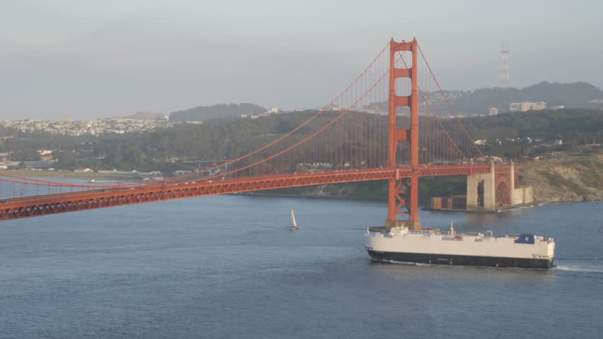 Freight ship sailing under the Golden Gate Bridge and city in background at sunset, San Francisco, California, USA