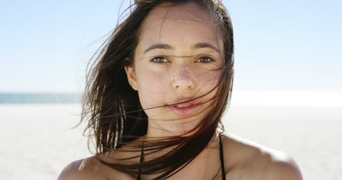 Close up portrait of beautiful young woman running hand through hair blowing in wind on tropical beach slow motion