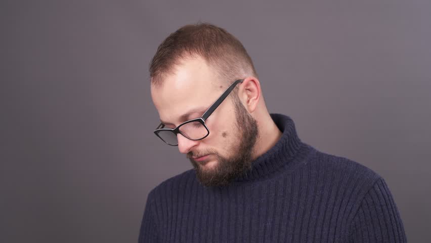 Close-up portrait of a bearded young man in glasses looking in camera with sorrow. Isolated on grey background. Royalty-Free Stock Footage #1020570433