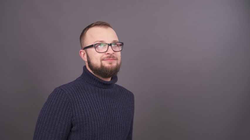 Close-up portrait of young bearded caucasian man in glasses bashfully looking up. Isolated on grey background. Royalty-Free Stock Footage #1020570481