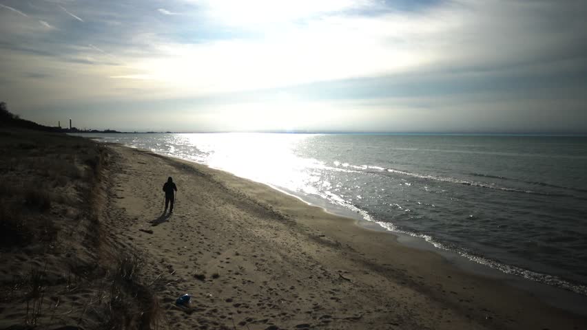 A pedestrian walks along the shore of the lake along the sand dunes