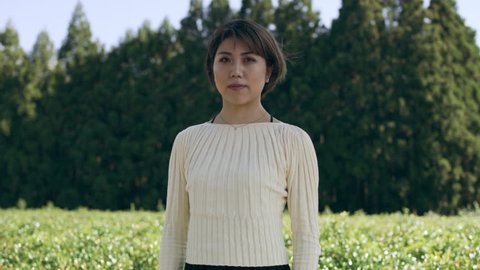 Zoom in Portrait of Japanese woman standing in front of tea plants and trees with soft natural lighting. Medium shot on 4k RED camera.