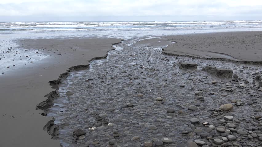 The shore of the Pacific Ocean, the rapidly flowing water of a small river flows along the beach, the Olympic National Park, USA, Washington
