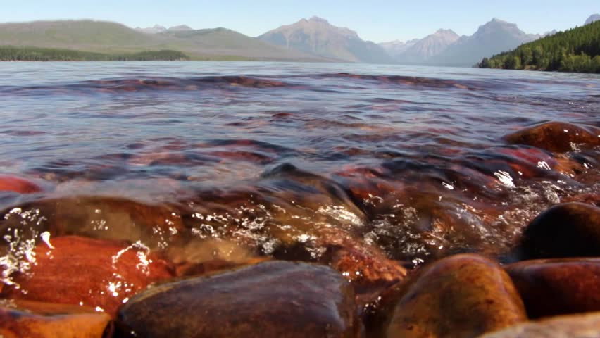 Low angle shot of the colorful rocks in Lake McDonald. Glacier National Park. Montana. USA. With sound of waves hitting the shore.