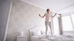 Young carefree woman in casual having fun and jumping with pillow on bed 