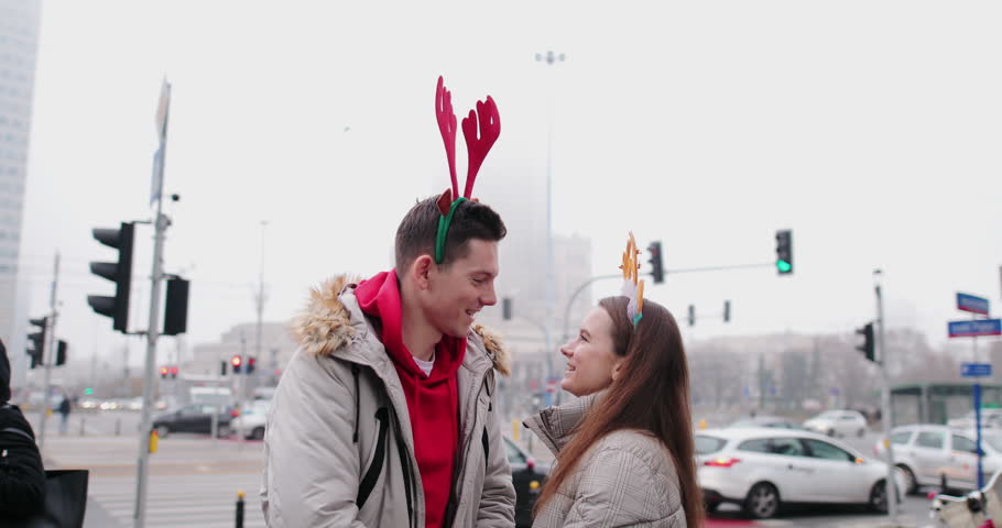 Lovely Couple standing on the street and wear Christmas horns on head. Smile to camera and give a hug