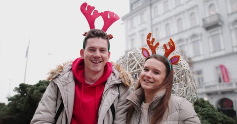 Lovely Couple standing on the street and wear Christmas horns on head. Smile to camera and give a hug