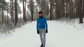 Aerial video of a lone runner in wintry wood. Drone flight over man running snow forest trail in winter. Active lifestyle, winter sports and marathon concept. Man jogging winter forest. 