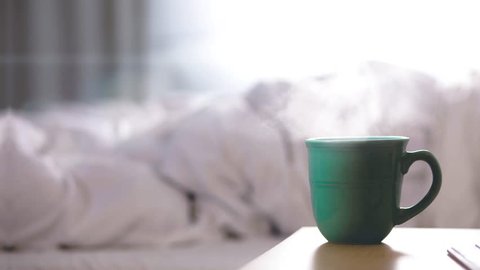 Hot cup of coffee on night table and messy bed 4K