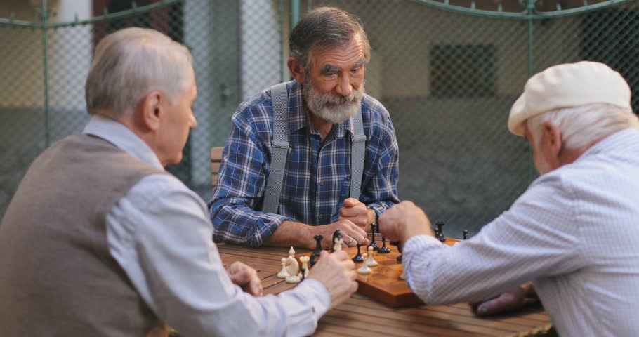 Old male friends playing chess in the yard. One man doing his turn and another one doing gesture like no turns anymore. Outdoor.