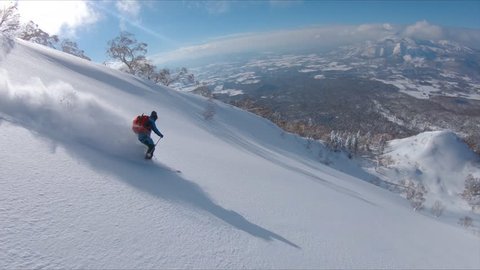 SLOW MOTION, DRONE: Awesome freestyle skier shredding the fresh snow while riding in the scenic mountains in Japan. Flying along the active male tourist skiing downhill in the breathtaking backcountry