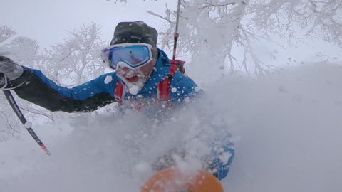 SLOW MOTION, SELFIE: Two cheerful male tourists having fun skiing in the untouched mountain terrain in Japan. Freeride skiers enjoying their winter vacation in Niseko by shredding fresh powder snow.
