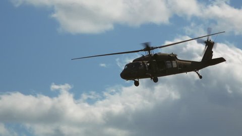 Military helicopter on battlefield flies overhead passing in slow-motion. Blackhawk chopper. Blue skies and clouds.