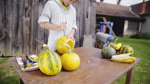 Zoom in while stabbing sharp knife in to empty pumpkin HD. Young person in woolen sweater on old farm working on making a Halloween pumpkin face with knife on brown table.