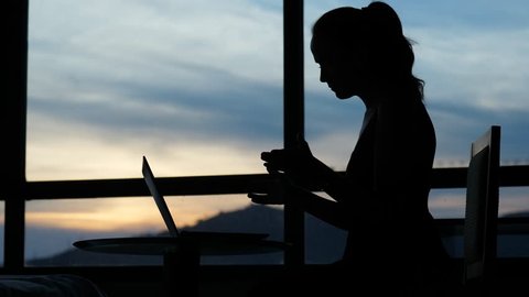 Woman disappointed with system or application error, laptop freeze-up, lady rise hands with indignation. Black silhouette of sitting girl against window, sunset sky seen blurred on background