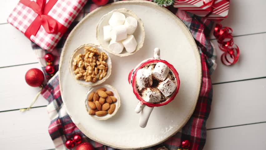Delicious homemade christmas hot chocolate or cocoa with marshmellows in a red xmas decorative cup. With almonds, walnuts in small bowls on side