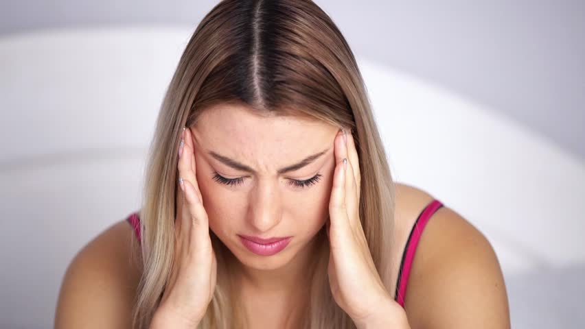 A girl’s headache, a woman has headache in different life circumstances, she clearly shows that she is in pain, clutches her head, a woman’s migraine, takes migraine pills, works on camera | Shutterstock HD Video #1020635071